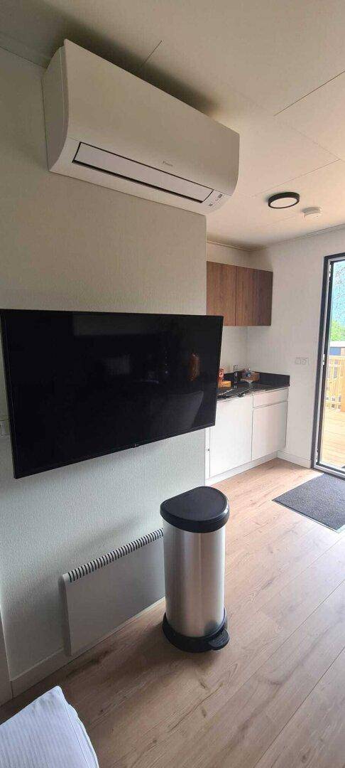 Wohnbereich mit Flachbildfernseher, Klimaanlage und Holzboden, offen zur Küche.