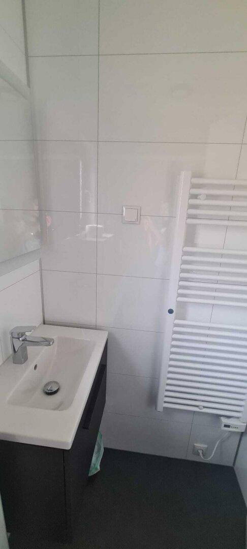 Helles Badezimmer mit Waschtisch, Spiegel und beheiztem Handtuchhalter an der Wand.