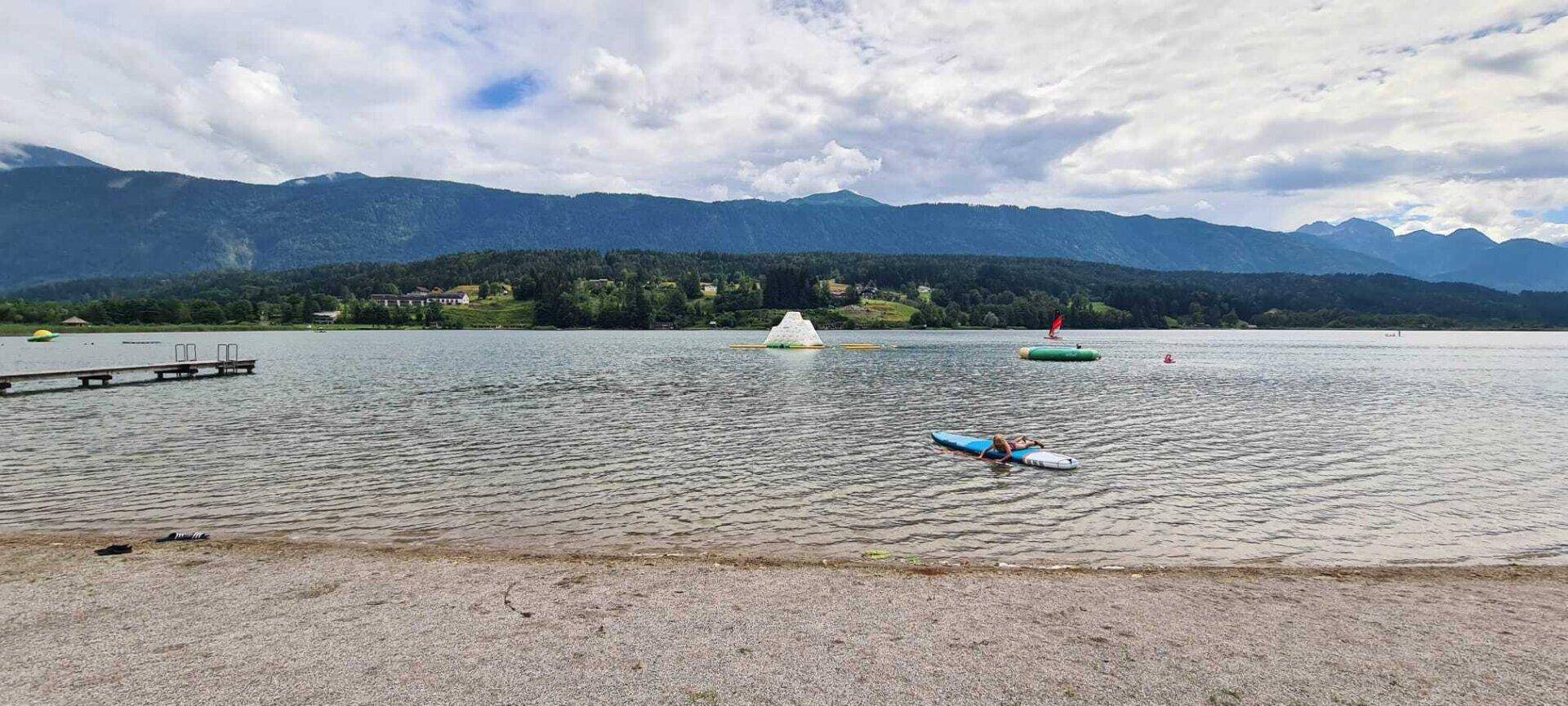 Weitläufiger See mit Bergpanorama, einem Steg und Wassersportmöglichkeiten.