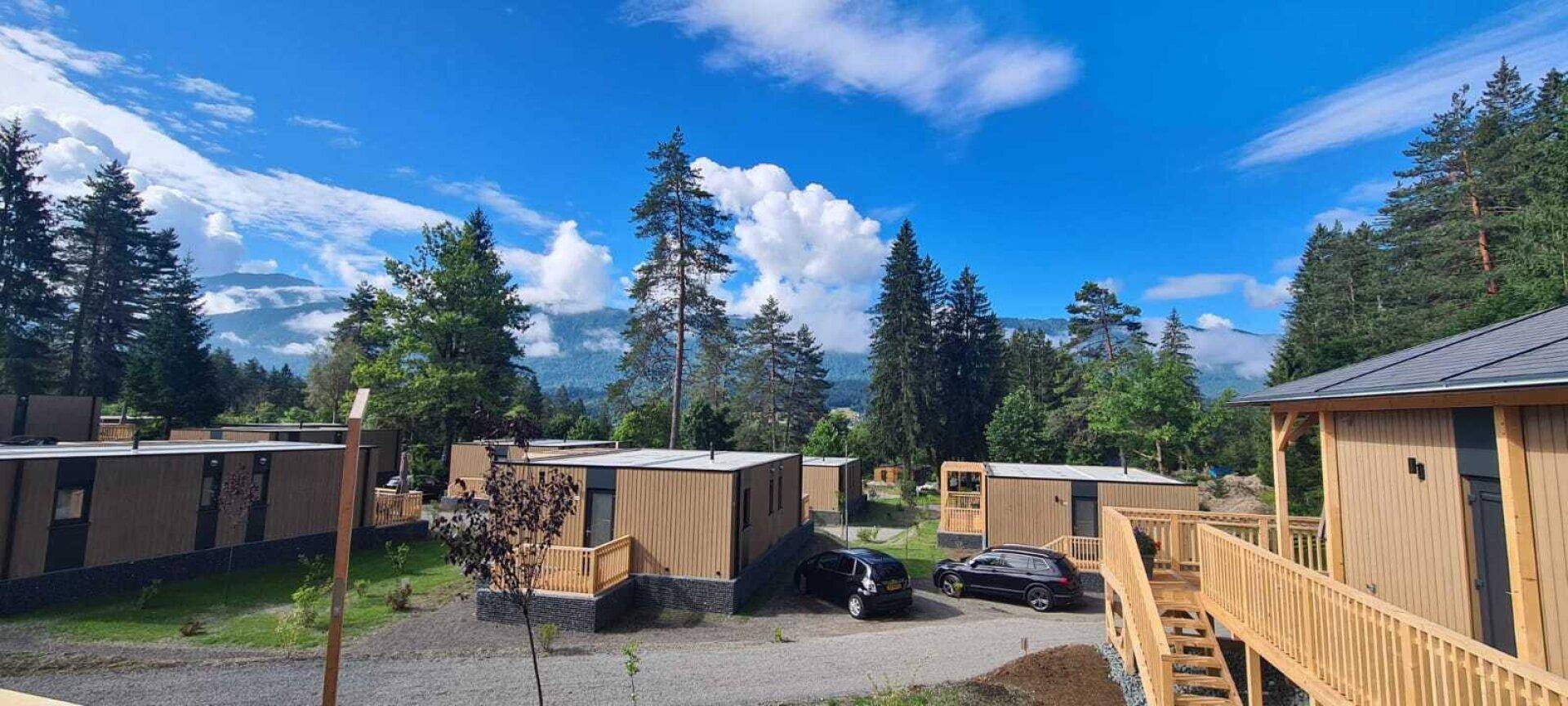 Ferienpark mit modernen Bungalows in einer grünen Umgebung mit Bergblick unter blauem Himmel.