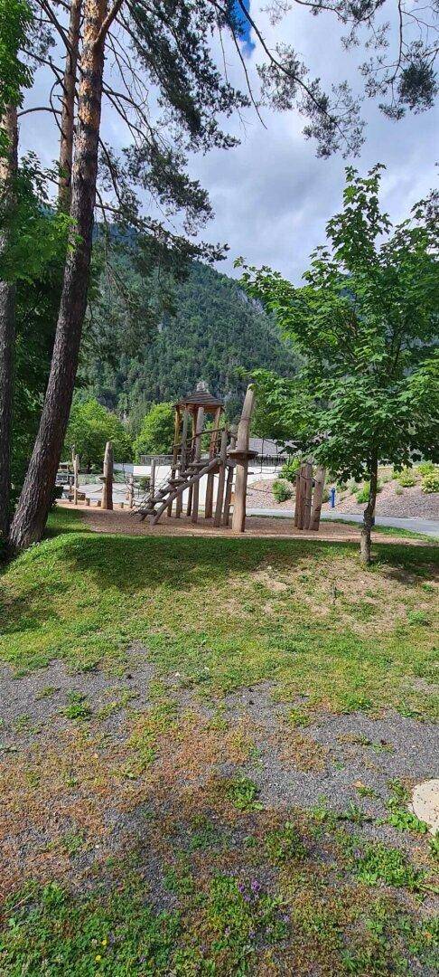 Naturnaher Spielplatz mit Holzelementen und Blick auf die umliegenden Berge im Hintergrund.
