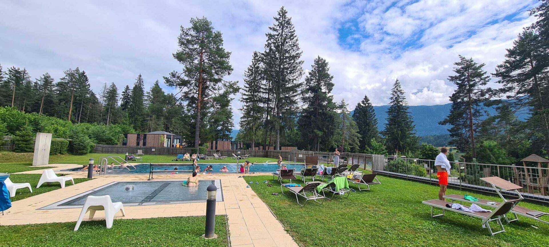 Entspannter Poolbereich mit Liegestühlen und Badegästen, umgeben von Bäumen und Natur.