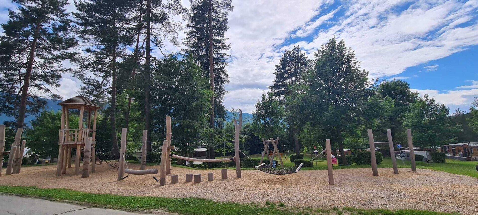 Großer Holzspielplatz mit verschiedenen Kletter- und Schaukelmöglichkeiten in natürlicher Umgebung.