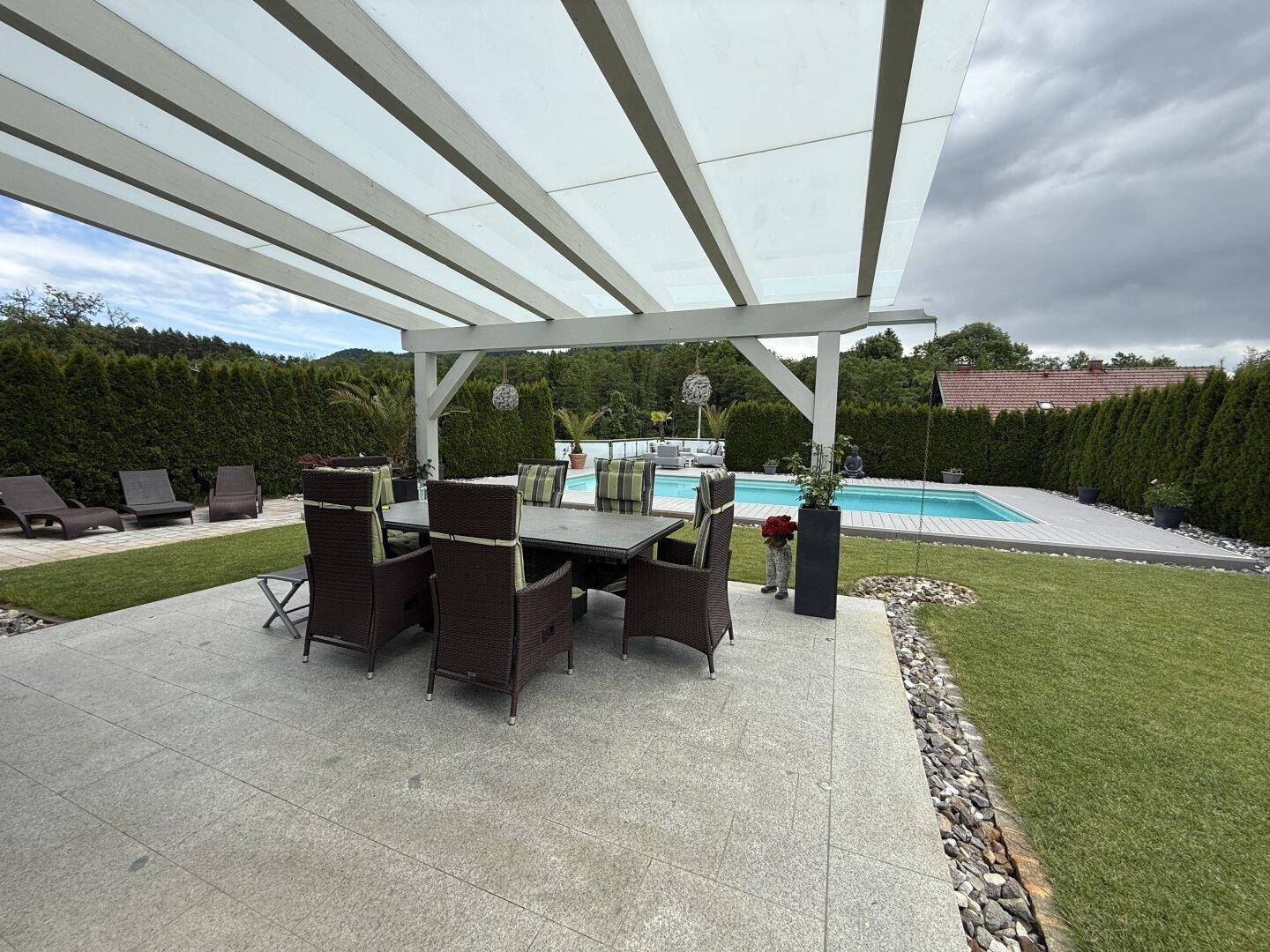 Überdachte Terrasse mit großem Esstisch und Stühlen, ideal für Mahlzeiten am Pool.