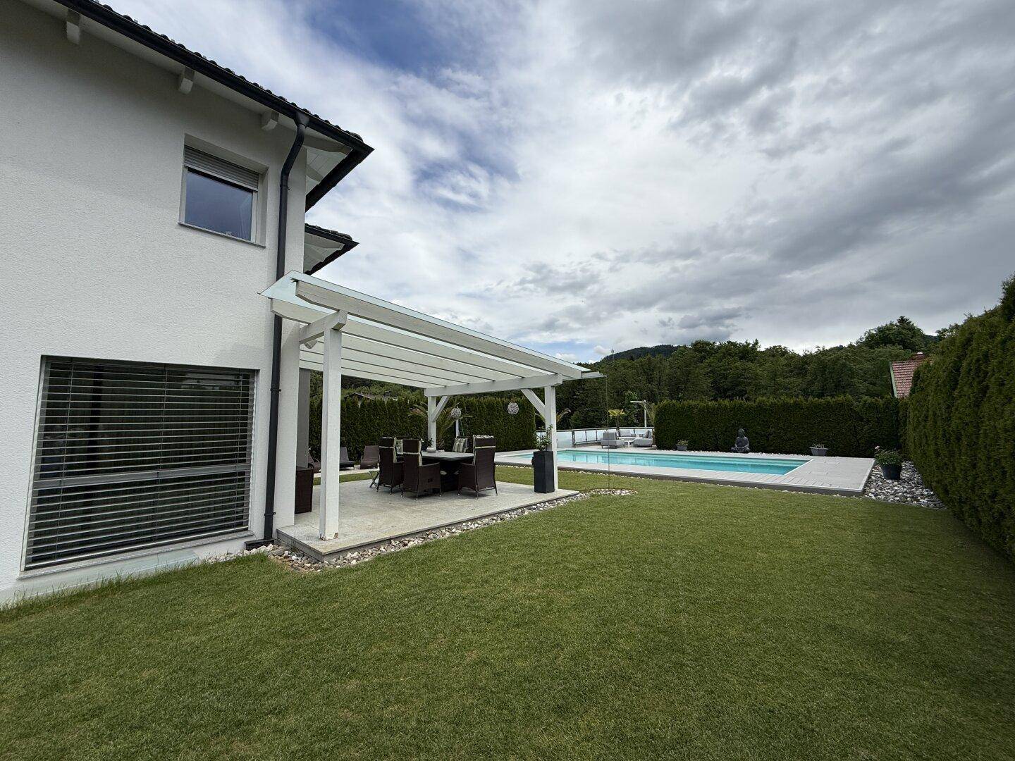 Moderne Hausfassade mit angrenzendem Garten, Pool und überdachtem Essbereich.