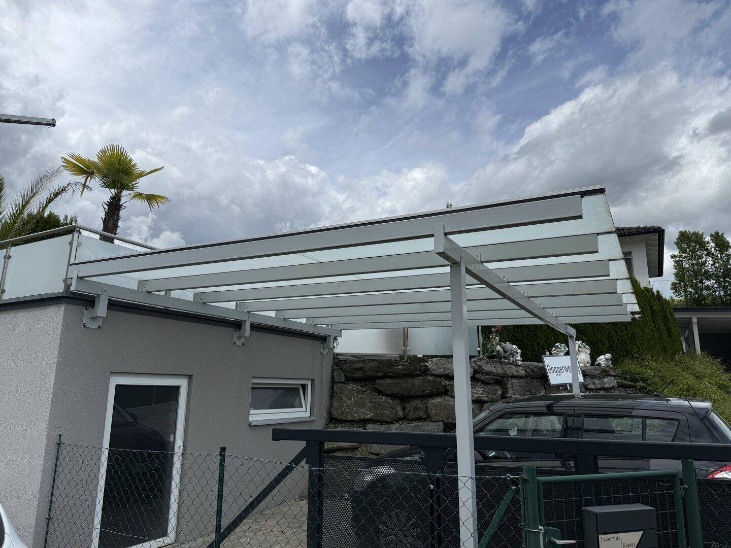 Moderner Carport mit Glasdach bietet geschützten Parkplatz neben dem Gebäude.