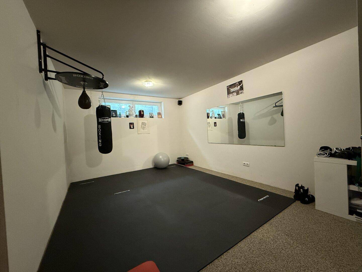Privater Fitnessraum mit Boxsack, Spiegel und Trainingsmatte für sportliche Aktivitäten.