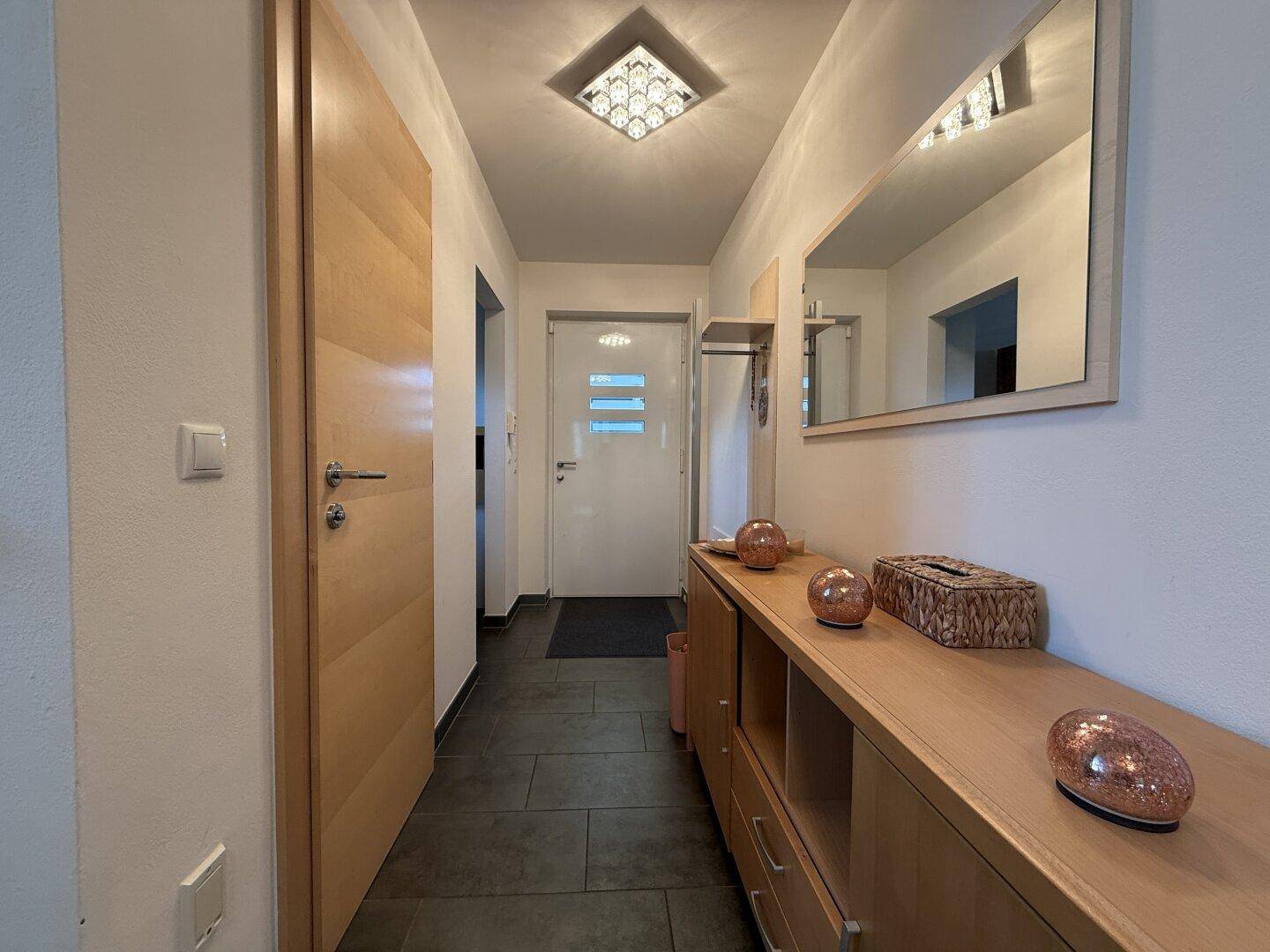 Heller Eingangsbereich mit Garderobe, Spiegel und praktischen Holzmöbeln.