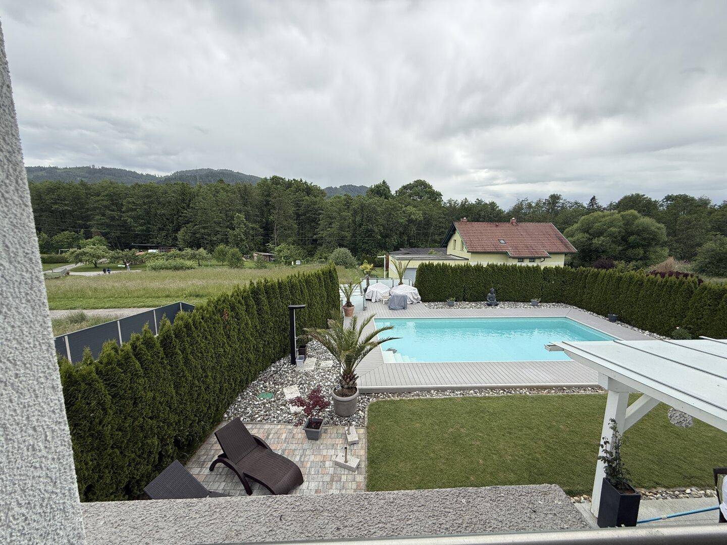 Weitläufiger Blick vom Balkon auf den Garten mit Pool und die grüne Umgebung.