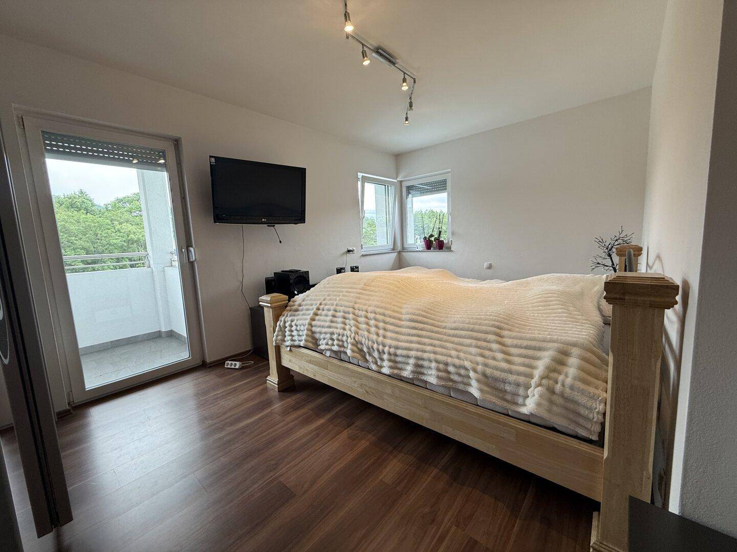 Helles Schlafzimmer mit Holzbett, Parkettboden und Zugang zum Balkon.