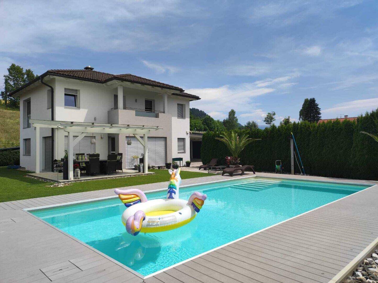 Modernes Haus mit großem Pool, gepflegtem Rasen und überdachtem Essbereich im Garten.