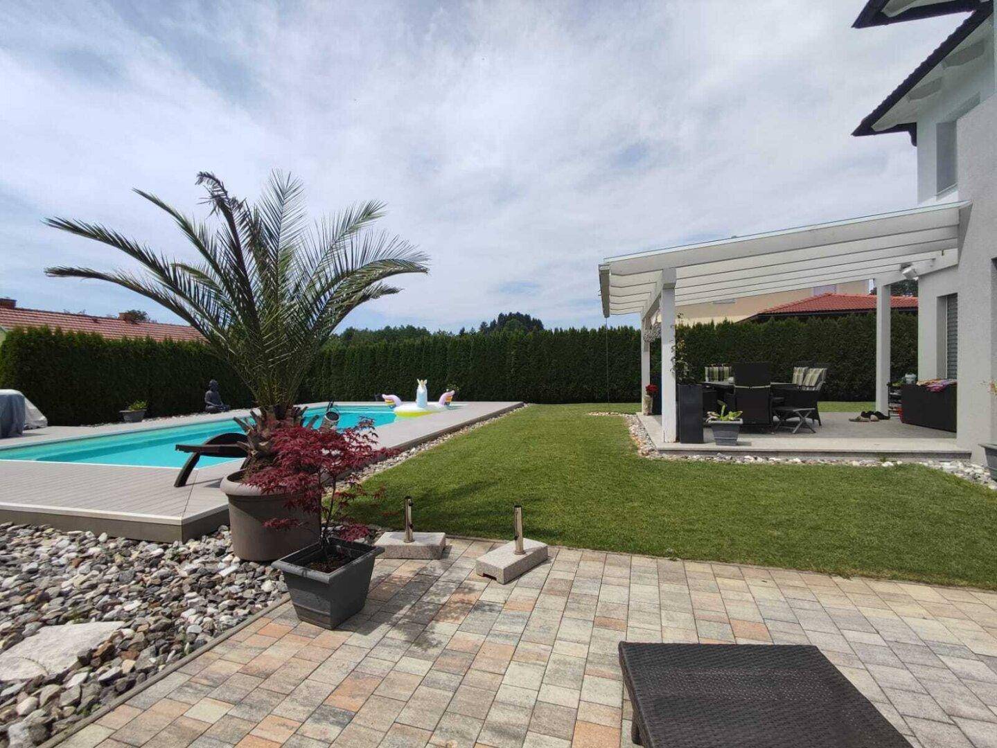 Attraktiver Garten mit Pool, Palmen und einer überdachten Terrasse für Mahlzeiten im Freien.