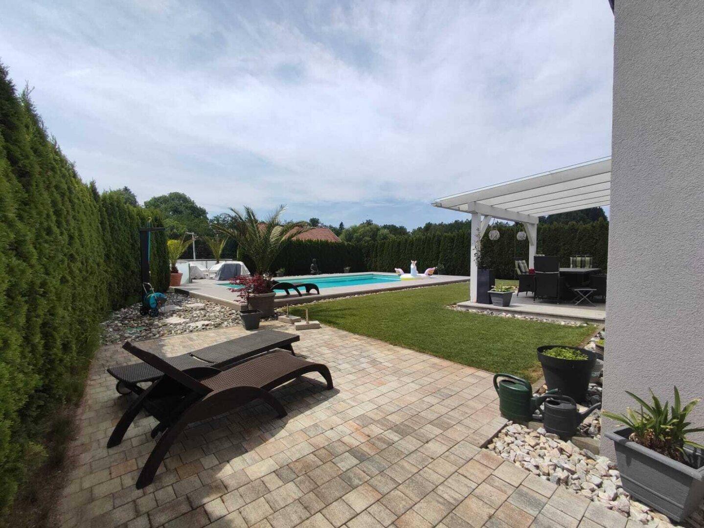 Gepflegter Garten mit Pool, Liegestühlen und einer hohen Hecke für Privatsphäre.