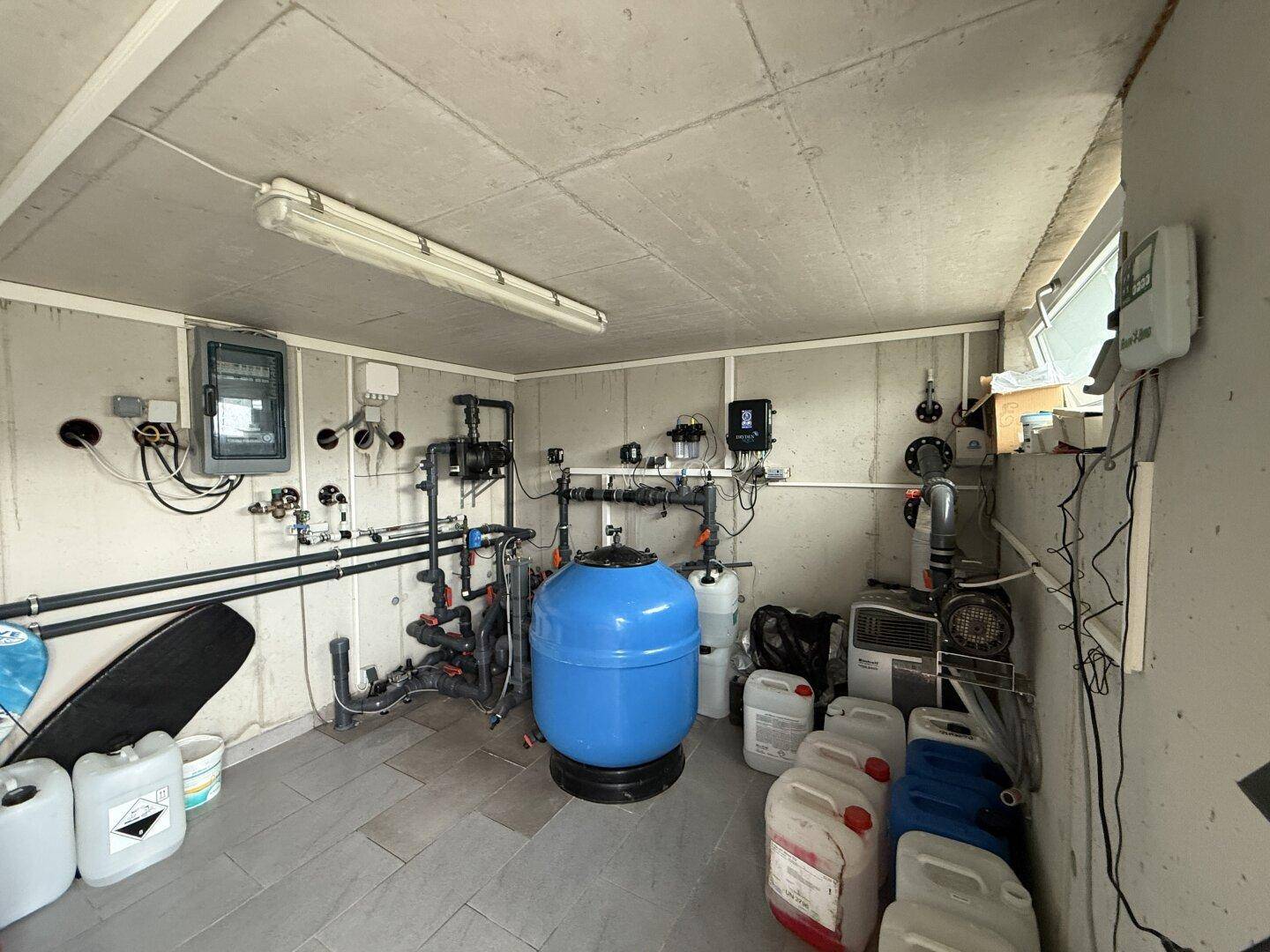 Technikraum mit Poolfilteranlage, Rohren und Lagerbehältern für die Poolpflege.