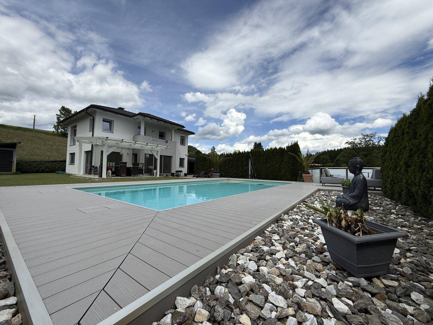 Modernes Haus mit weitläufigem Garten, großem Pool und dekorativen Steinelementen.