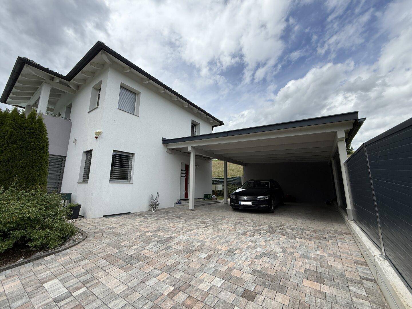 Modernes Einfamilienhaus mit geräumigem Carport und gepflasterter Auffahrt.