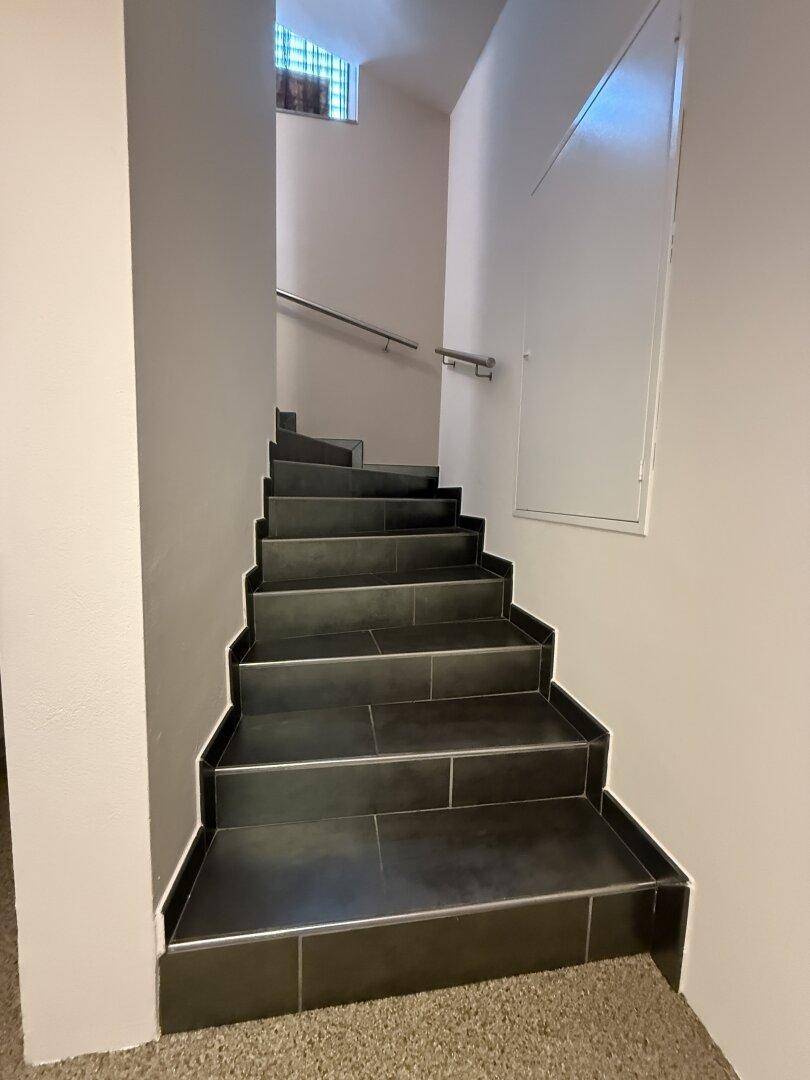 Treppenhaus mit dunklen Fliesenstufen und schlichtem Handlauf.