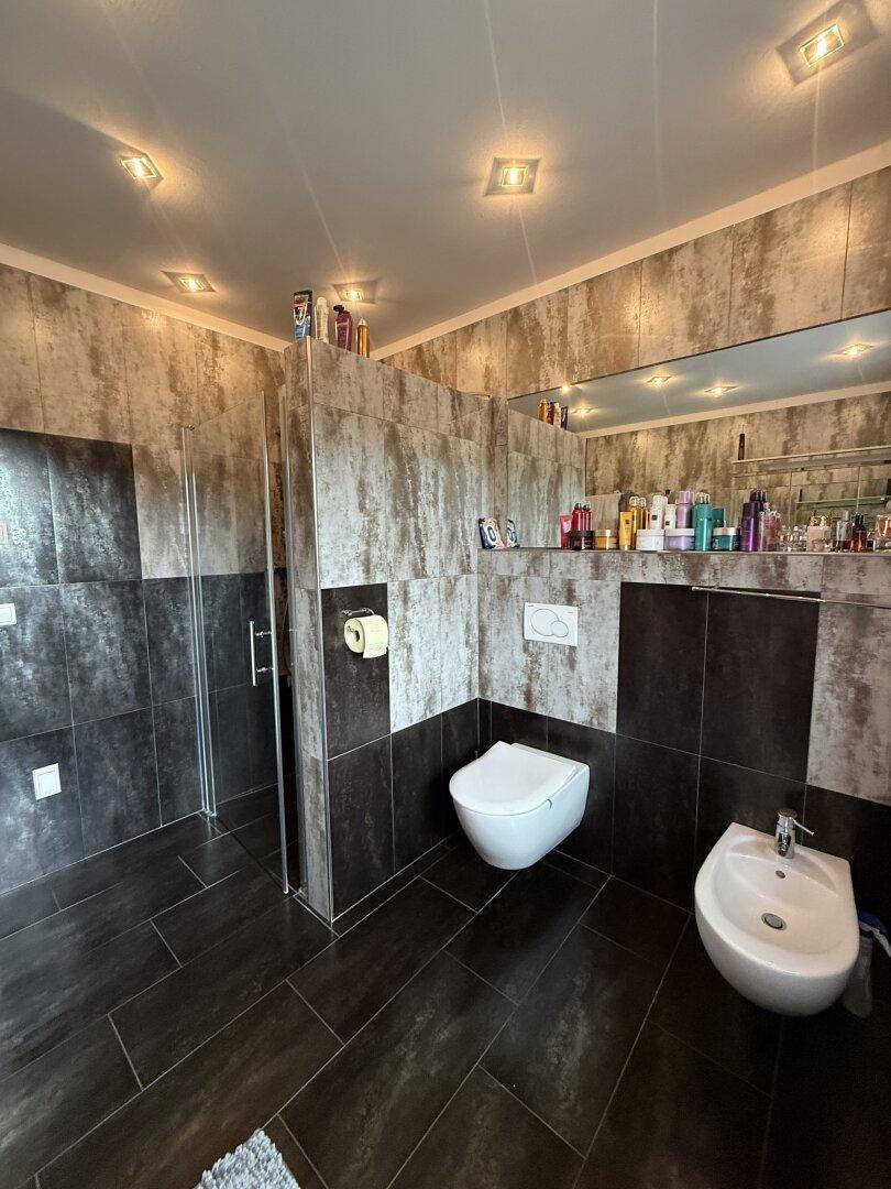 Stilvolles Badezimmer mit Duschkabine, Wand-WC und Bidet in dunklen Fliesen.