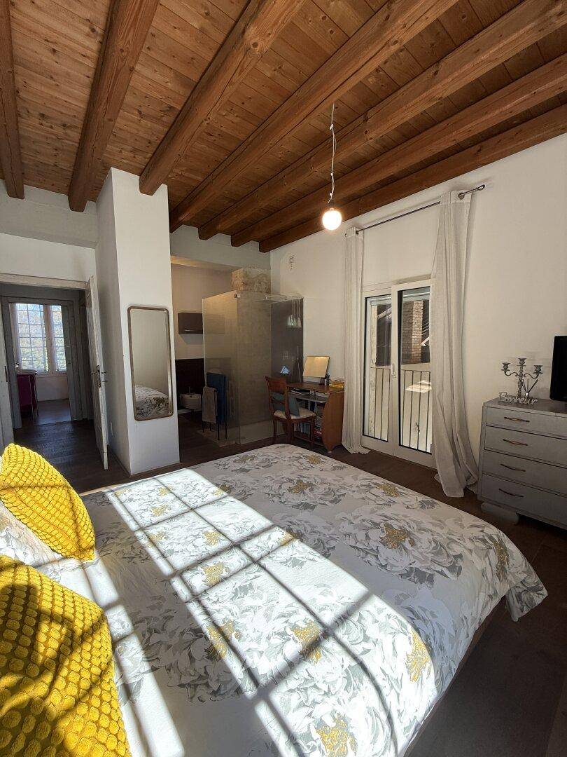 Schlafzimmer mit Holzbalkendecke, Parkettboden und Zugang zu einem französischen Balkon.