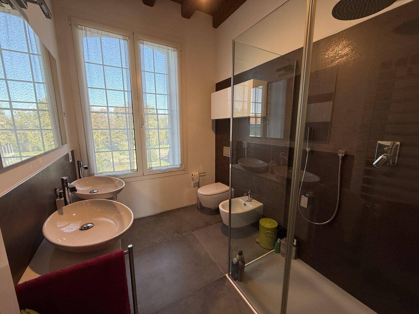 Geräumiges Badezimmer mit zwei Aufsatzwaschbecken, begehbarer Dusche und Fenster.