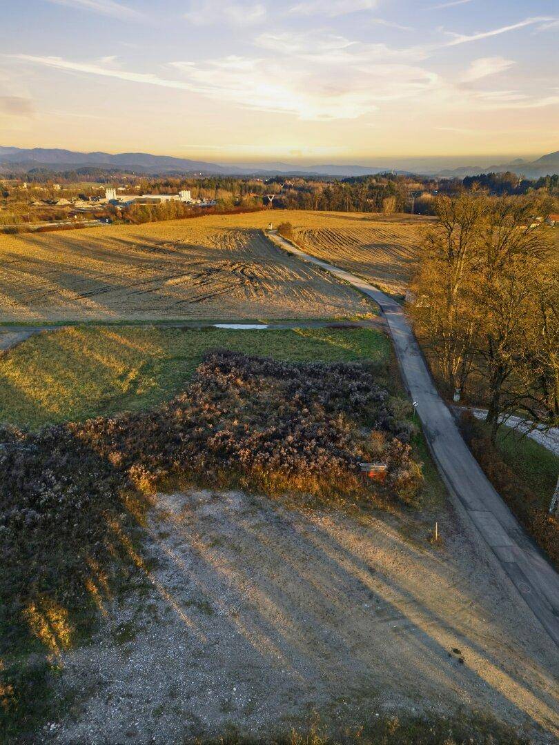 Weitläufige Felder und eine Landstraße bei Sonnenuntergang, mit Bergen am Horizont.