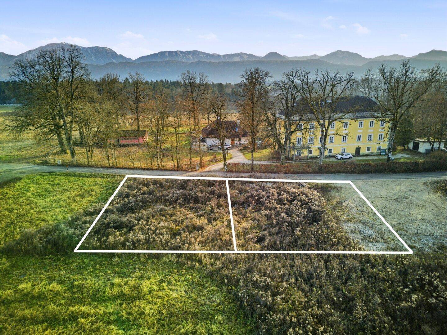Weitläufiges Baugrundstück mit markierten Grenzen, umgeben von Feldern und Bergen am Horizont.