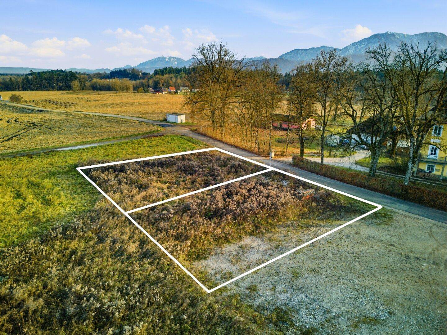 Luftbild eines Grundstücks mit markierten Parzellen, angrenzend an eine Straße und weite Felder.