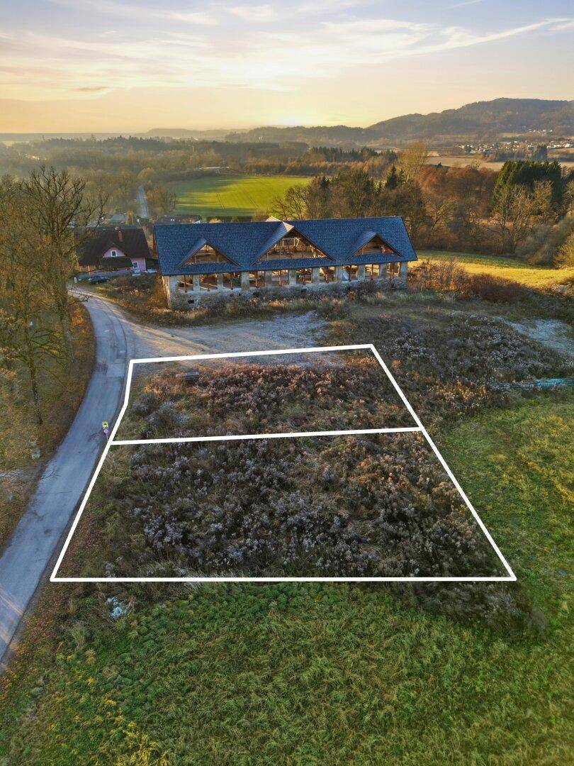 Luftaufnahme eines Baugrundstücks mit markierten Grenzen, umgeben von Feldern und einem Gebäude.