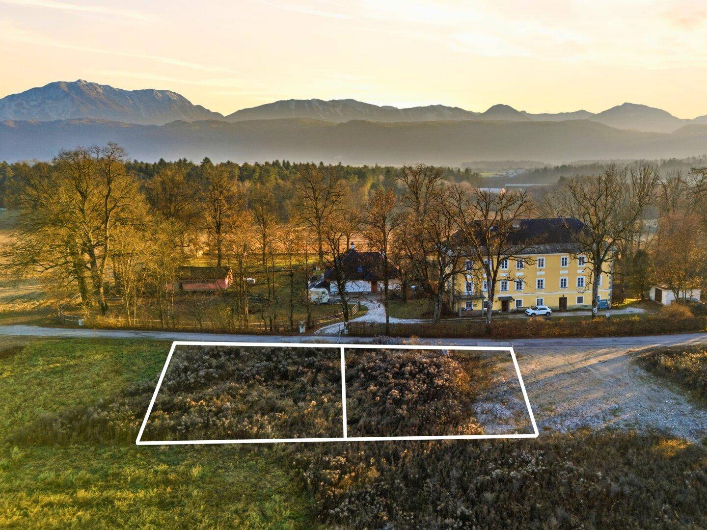 Luftaufnahme eines Baugrundstücks mit markierten Grenzen, umgeben von Natur und Bergen.