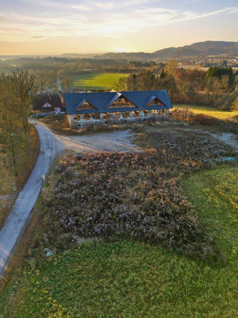Weitläufige Landschaft mit einem Gebäude im Hintergrund und grünen Feldern unter einem warmen Himmel.