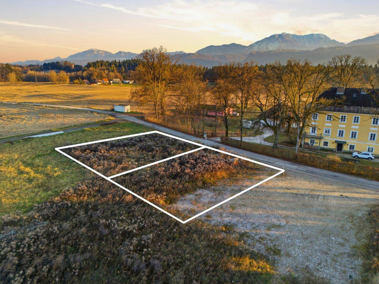 Luftbild eines Grundstücks mit markierten Parzellen, angrenzend an eine Straße und weite Felder.