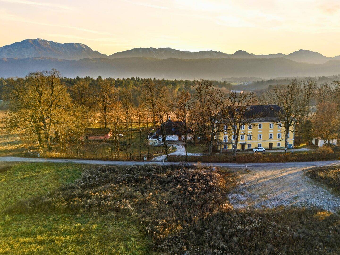 Weitläufige Landschaft mit historischen Gebäuden im Hintergrund und grünen Feldern unter blauem Himmel.