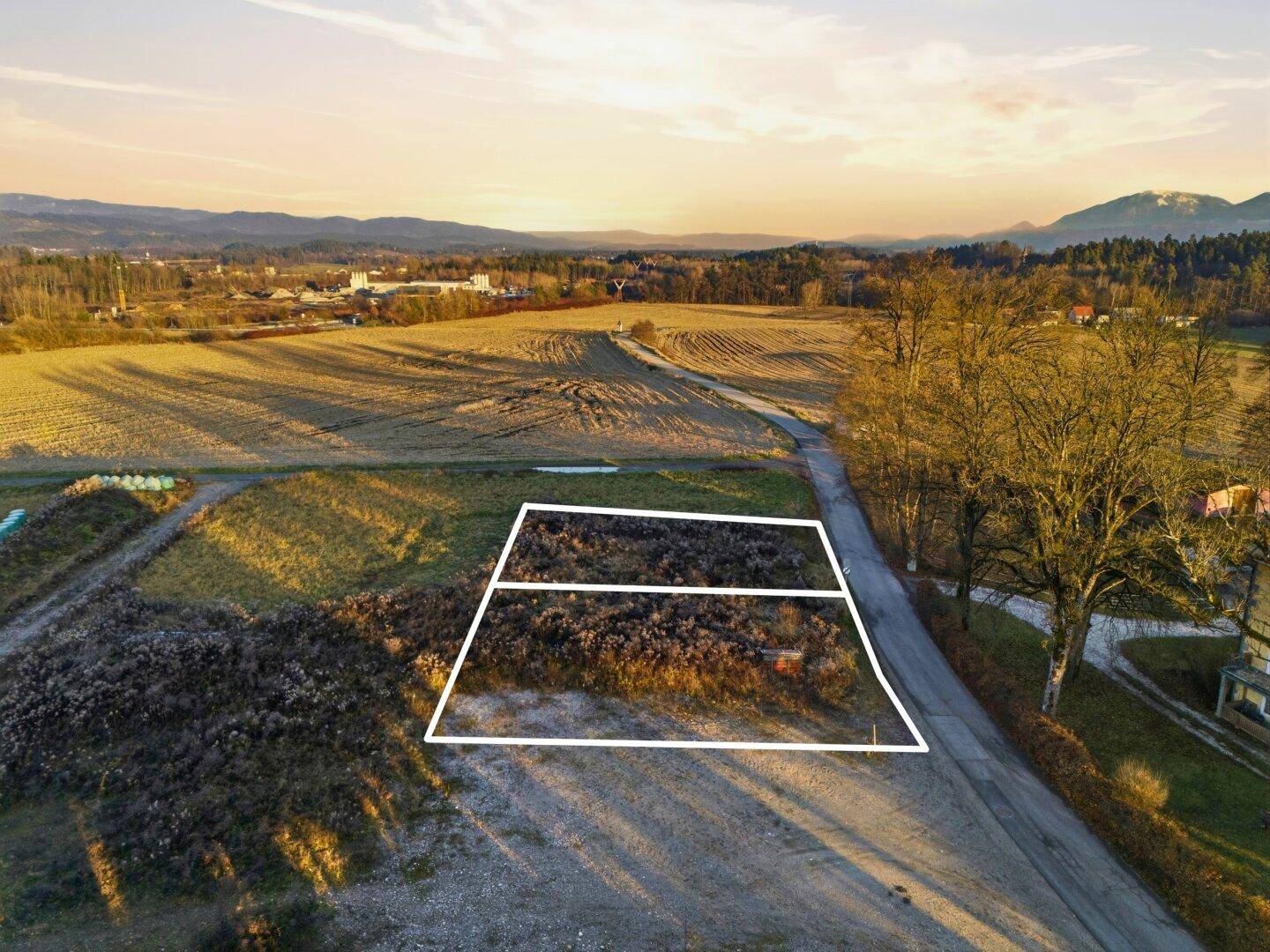 Luftbild eines Grundstücks mit markierten Parzellen, angrenzend an eine Straße und weite Felder.