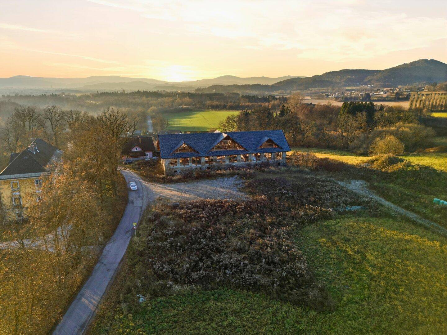 Weitläufige Landschaft mit einem Gebäude im Hintergrund und grünen Feldern unter einem warmen Himmel.