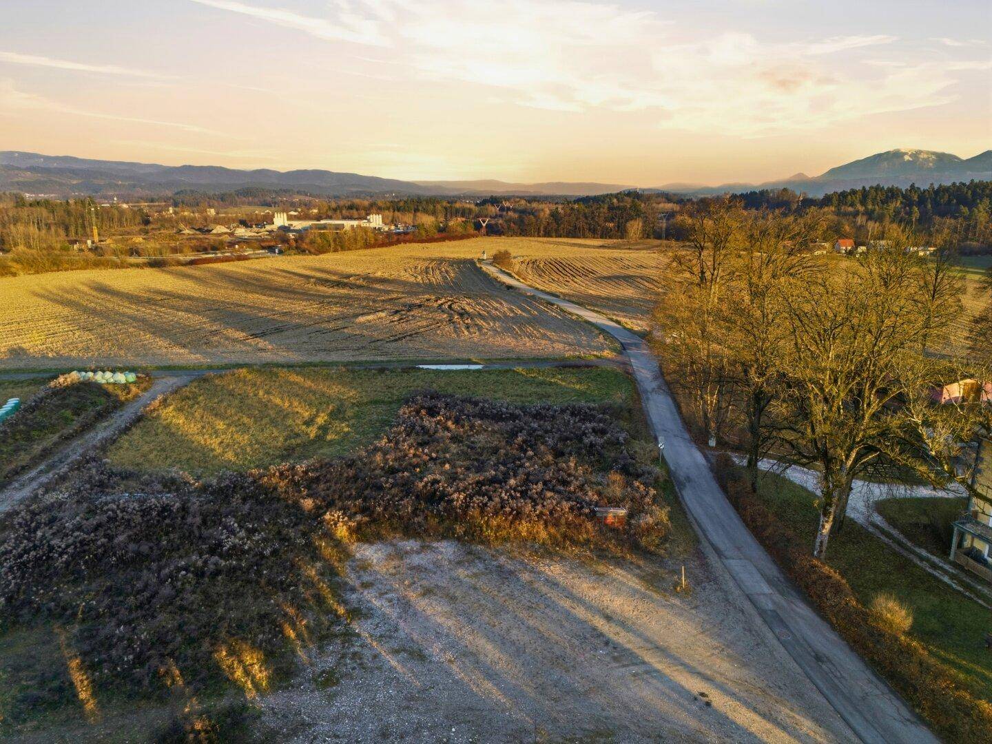 Weitläufige Felder und eine Landstraße bei Sonnenuntergang, mit Bergen am Horizont.