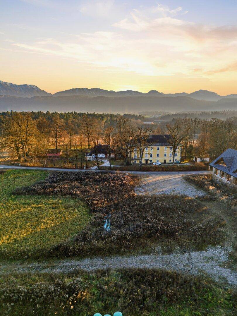 Weitläufige Landschaft mit historischen Gebäuden im Hintergrund und grünen Feldern unter blauem Himmel.