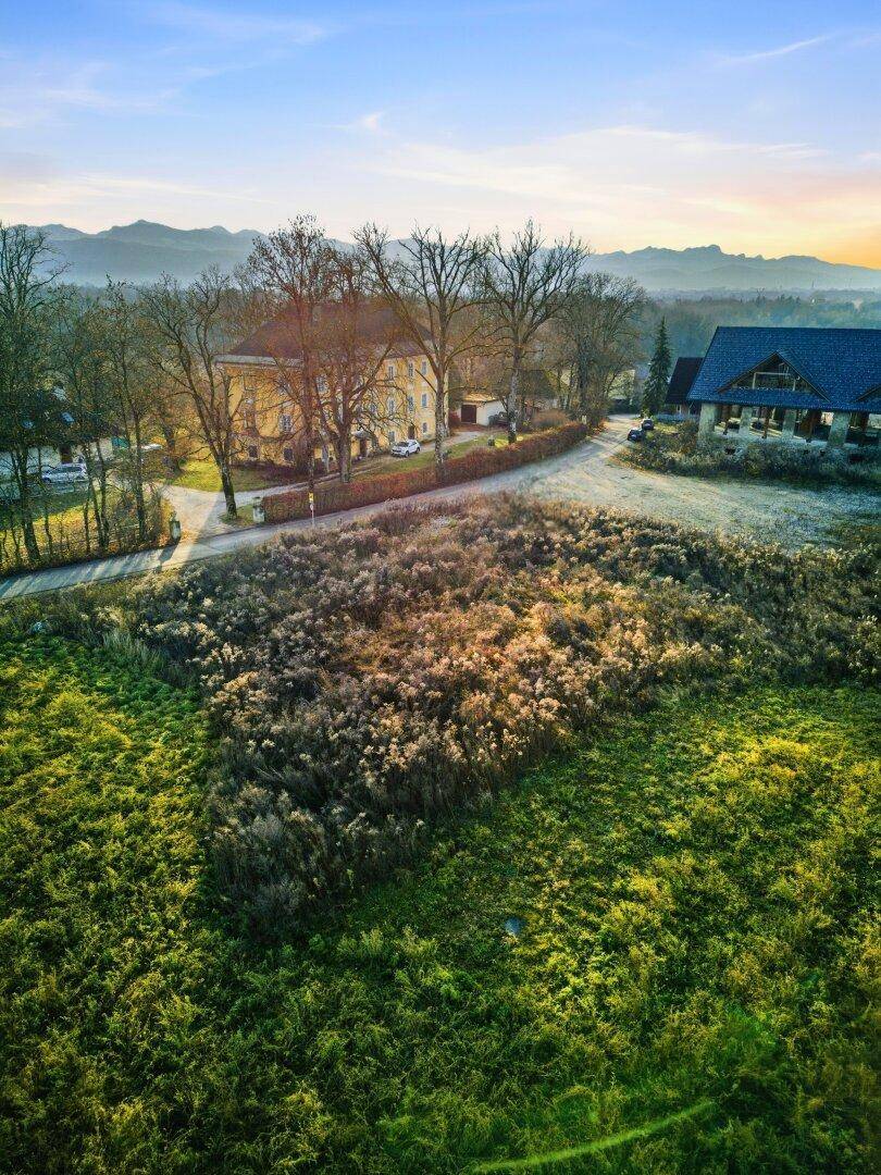 Weitläufige Landschaft mit historischen Gebäuden im Hintergrund und grünen Feldern unter blauem Himmel.