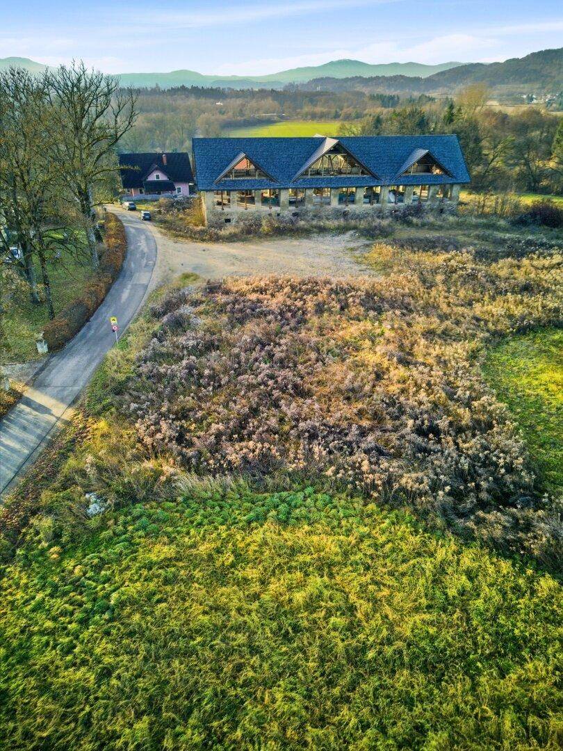 Weitläufige Landschaft mit einem Gebäude im Hintergrund und grünen Feldern unter blauem Himmel.