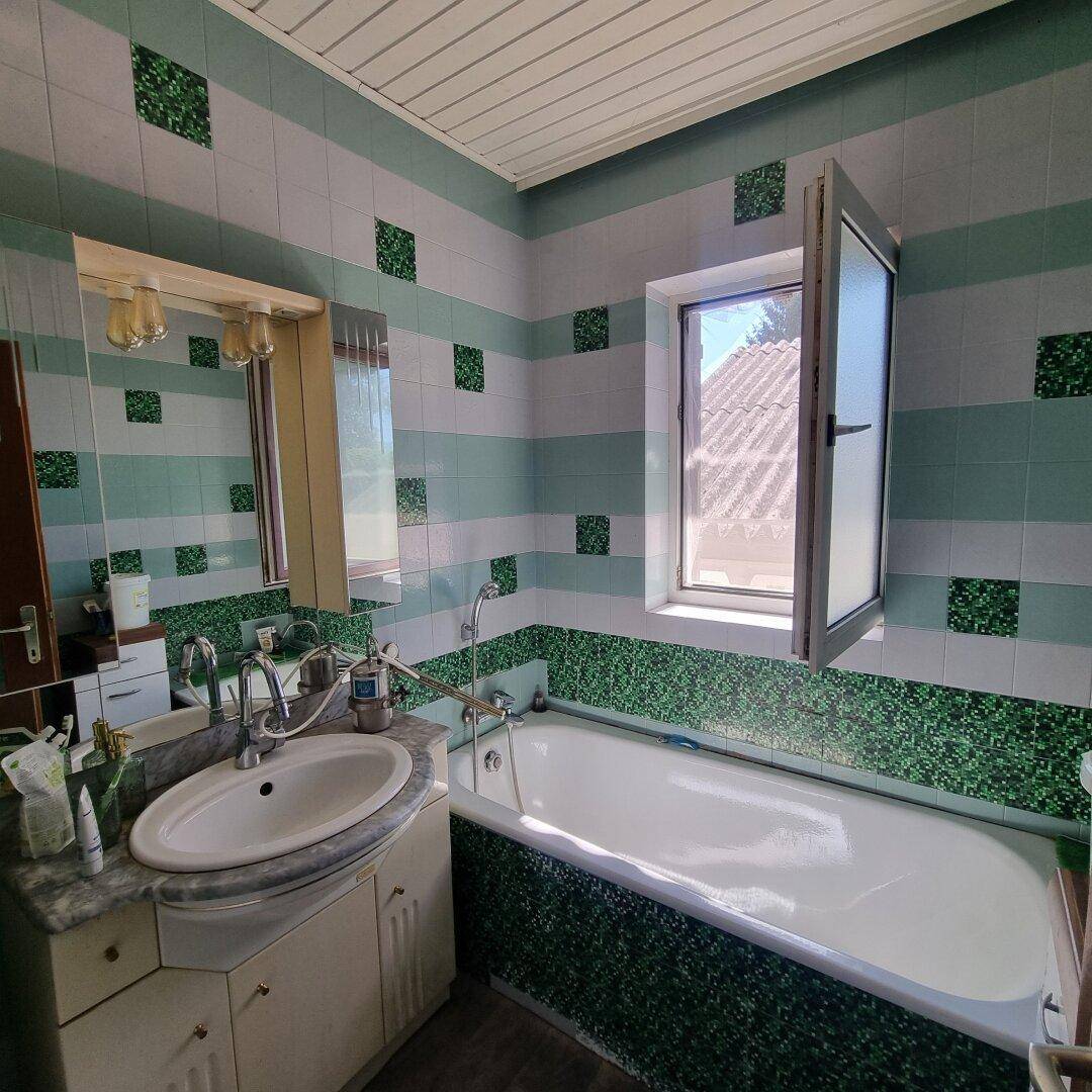 Badezimmer mit Badewanne, Waschbecken und farbigen Fliesen in Grün- und Weißtönen.
