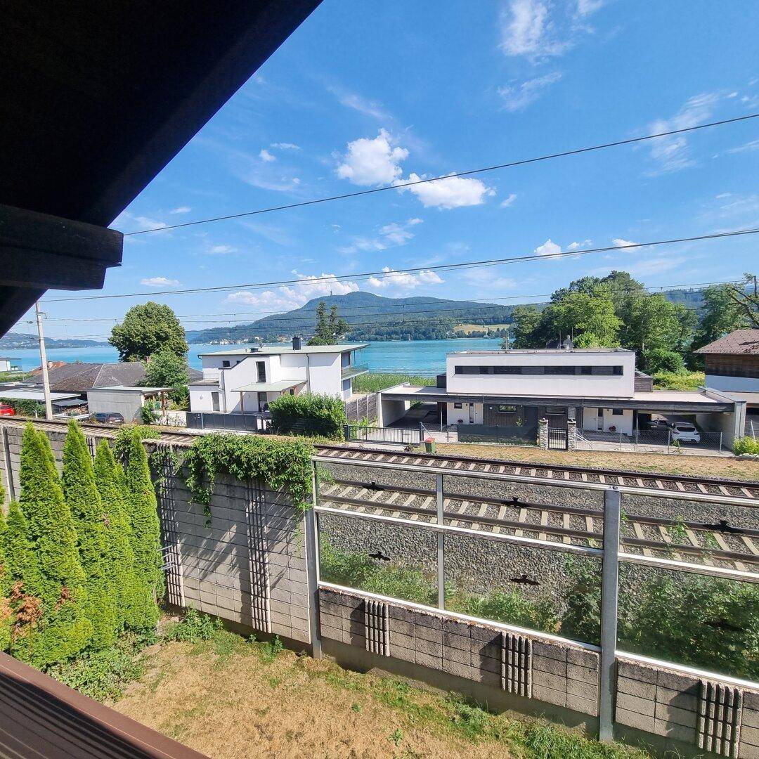 Blick vom Grundstück auf den See, mit Bahngleisen und modernen Häusern im Vordergrund.