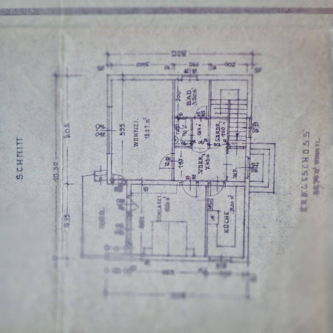 Grundriss des Erdgeschosses mit Wohnzimmer, Küche und Bad, detailliert dargestellt.