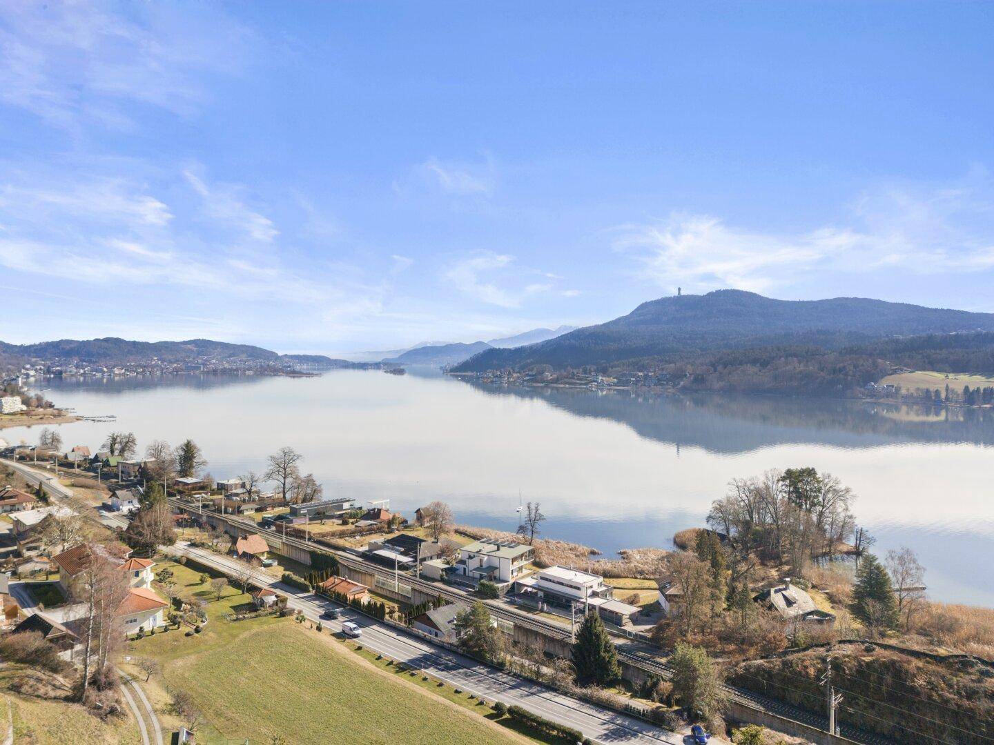 Weitläufiger Blick über den See mit bewaldeten Hügeln und Siedlungen am Ufer unter klarem Himmel.