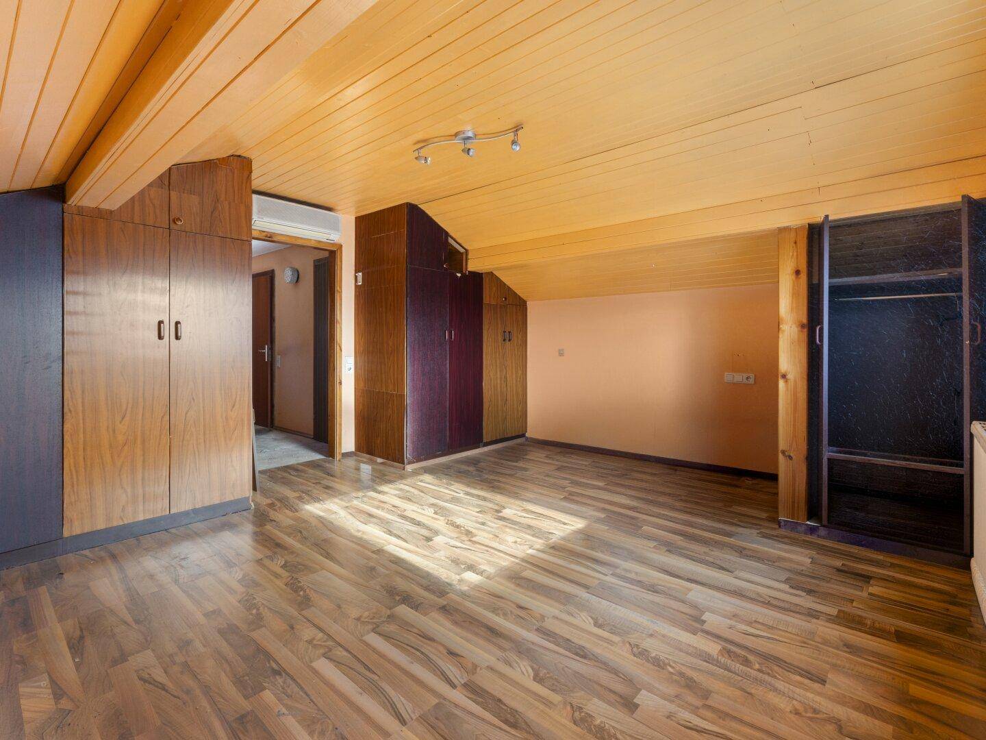 Geräumiges Zimmer mit Holzdecken, Laminatboden und integrierten Kleiderschränken.