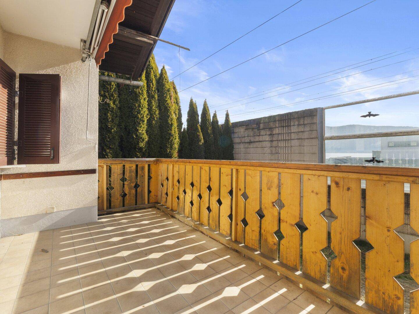 Geräumiger Balkon mit Fliesenboden und Holzbalkongeländer, sonnig gelegen mit Blick ins Grüne.
