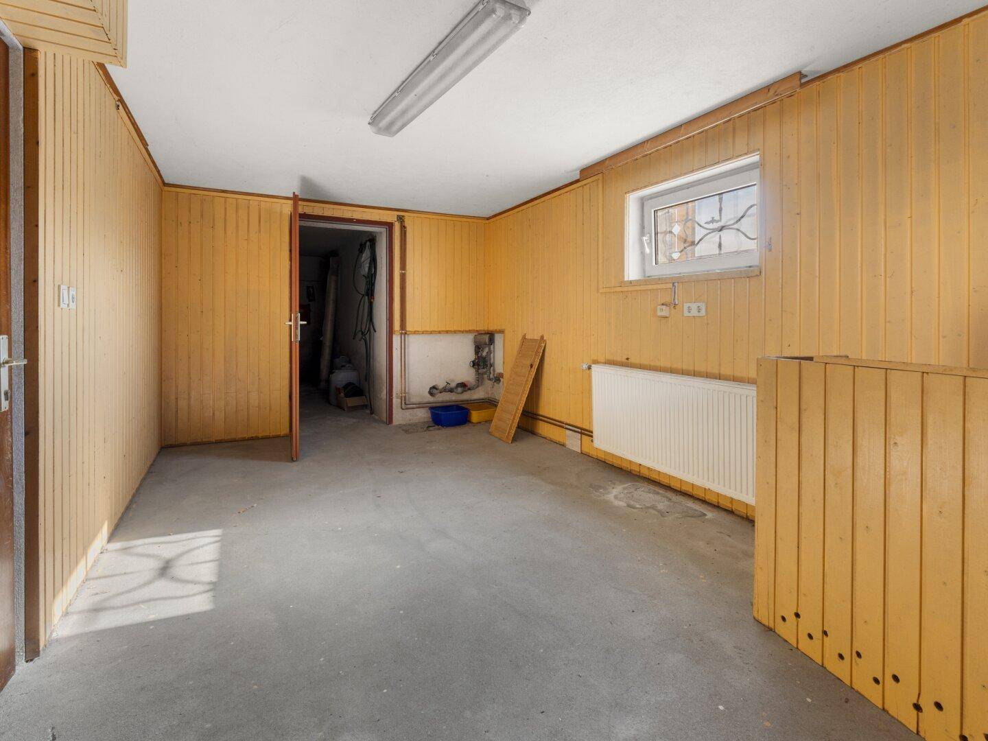 Funktionaler Raum mit Holzvertäfelung, Betonboden und Fenster für Tageslicht.
