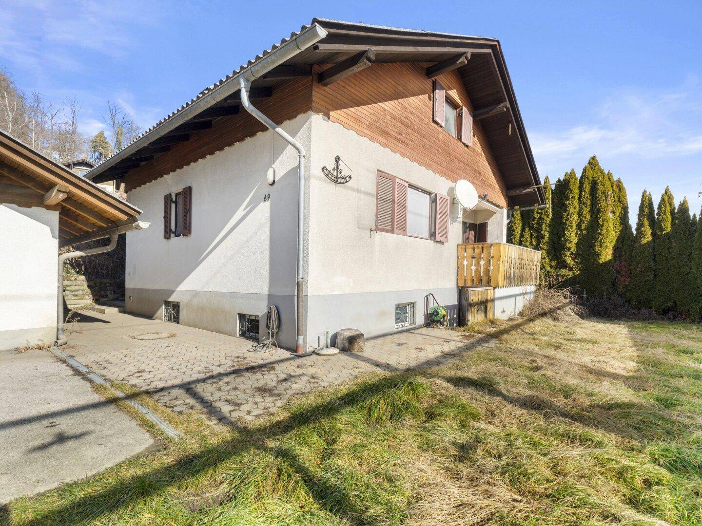 Seitenansicht des Hauses mit kleinem Balkon und Zugang zum Gartenbereich an einem sonnigen Tag.
