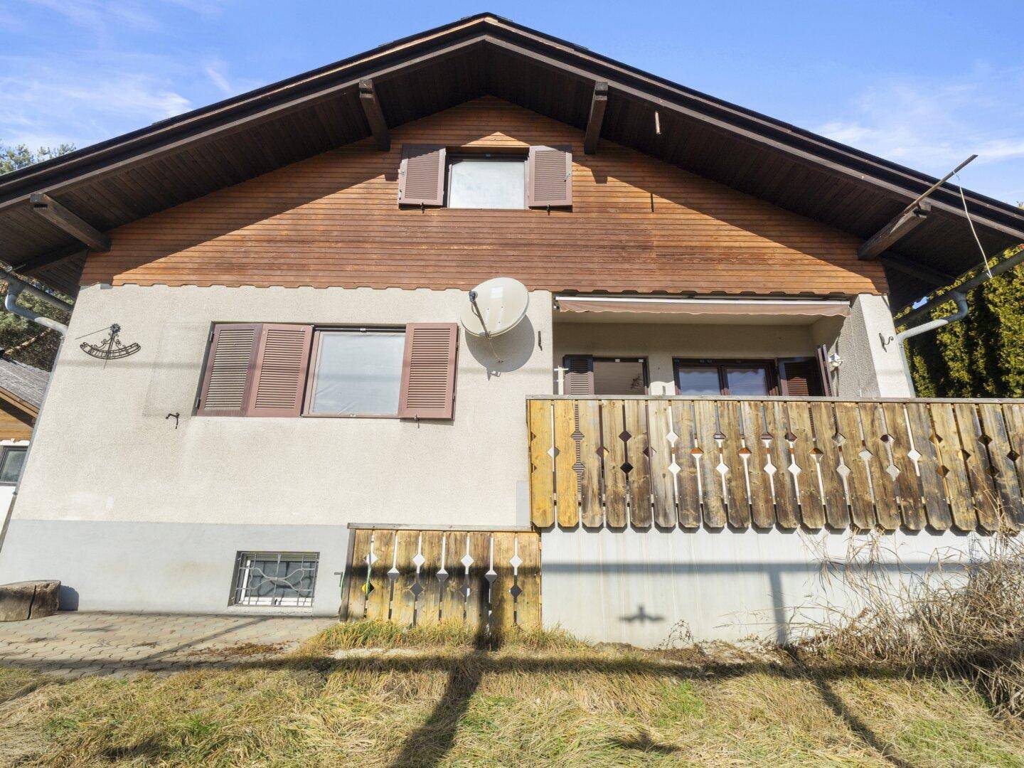 Vorderansicht des Hauses mit traditionellem Holzbalkon und Fensterläden unter blauem Himmel.