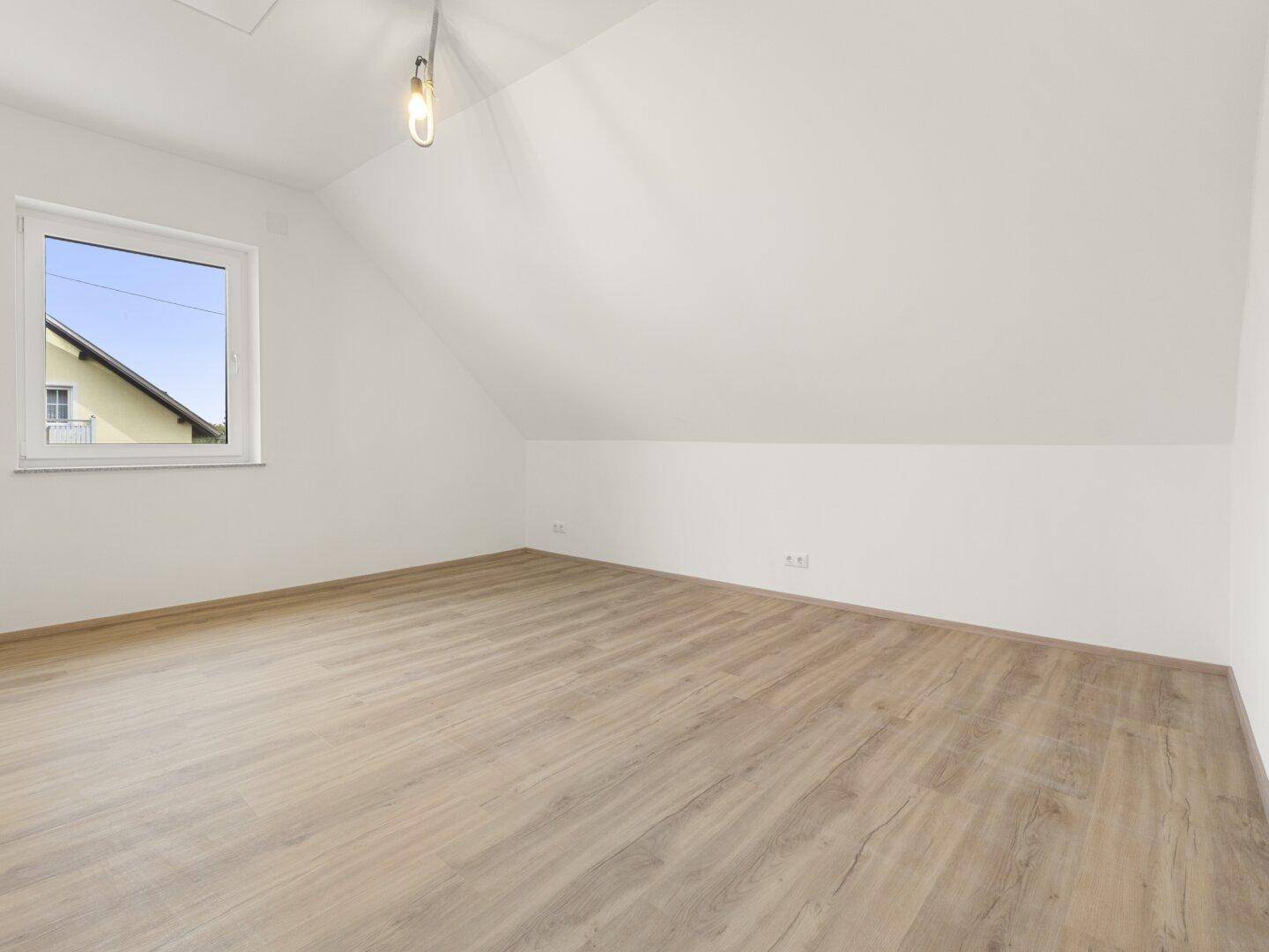 Helles Schlafzimmer im Dachgeschoss mit Laminatboden, schrägen Wänden und Blick nach draußen.