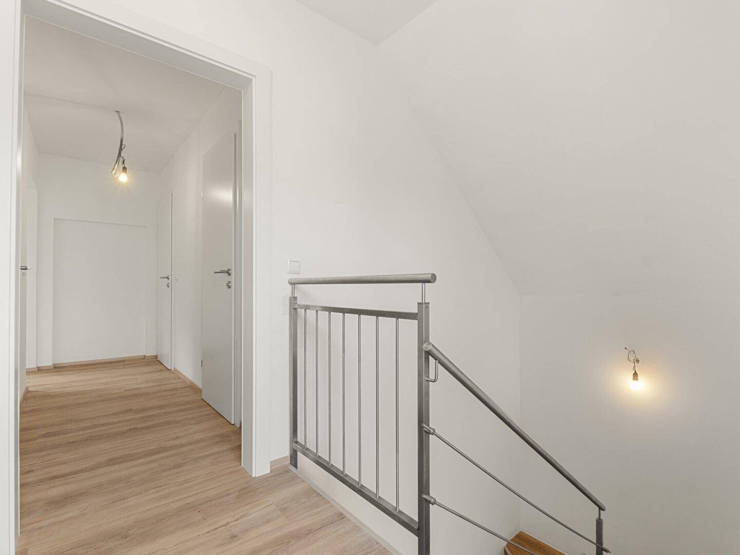 Heller Flur mit Laminatboden und modernem Treppengeländer, der zu weiteren Räumen führt.
