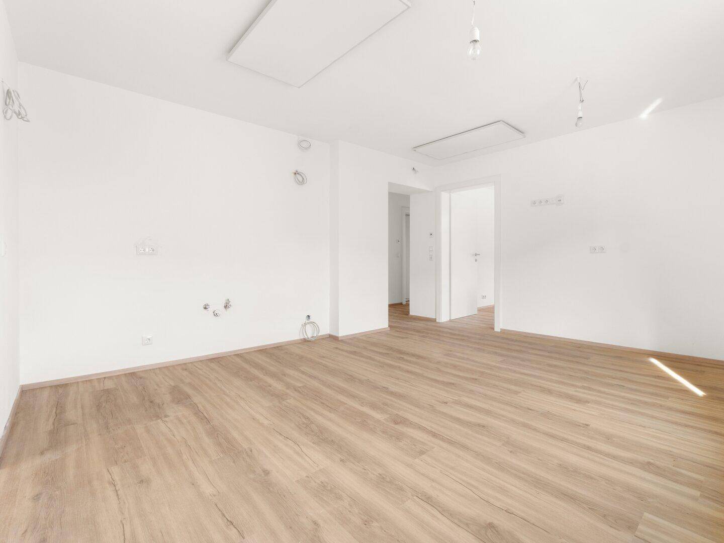 Leerer Küchenbereich mit Laminatboden und vorbereiteten Anschlüssen für eine Einbauküche.